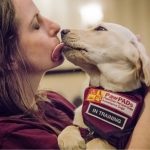 “Woman holds a vest-wearing, in-training assistance dog from PawPADs.